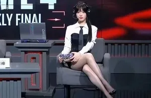 女解说员身穿全黑紧身衣、黑色长发,面部完全涂黑,坐在《永劫无间》解说席前,背景可见游戏相关屏幕和设备。