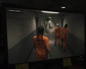 一张疑似《GTA6》的游戏截图,画面中一名深色短发女性角色(标注为露西娅)身穿橙色囚服,在监狱铁丝网围栏边奔跑,背景可见灰色砖墙与监控摄像头。