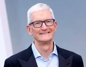 约翰·特努斯的官方肖像照,中年男性,身穿深色西装和浅色衬衫,面带微笑,背景为简洁浅灰渐变色。