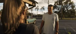一张疑似《GTA6》的游戏截图,画面中一名深色短发女性角色身着橙色囚服,在昏暗室内持金属棒状物面向铁门,背景可见监舍栏杆和‘PRISON’字样标识