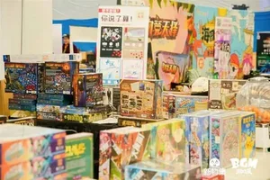 新物集BGM游戏展上海站现场照片:多人围站在一个布置有‘新物好奇集’标识的展区内,展台陈列多款彩色软胶捏捏玩具和潮流手办,观众正在驻足观看或挑选。