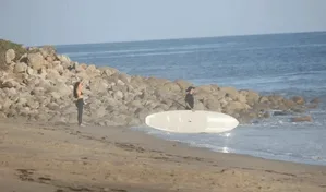 金·卡戴珊与刘易斯·汉密尔顿在加州马里布海滩海中相拥亲吻,卡戴珊穿黑色比基尼上衣和潜水服,汉密尔顿穿黑色T恤和短裤。