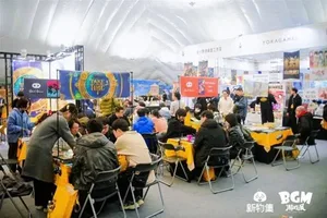 新物集BGM游戏展上海站现场,多人围站在一个摊位前专注试玩一款独立游戏,屏幕上显示游戏画面,摊位标有品牌标识和游戏名称。